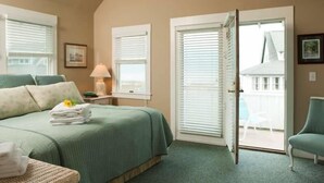 A bedroom with a bed, a nightstand, a lamp, a chair, and a sliding glass door to a balcony. - Purrfect Paws 2 Bedroom Holiday Home By Bald Head Island (Bald Head Island)