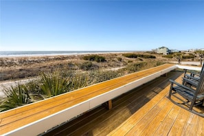 Une terrasse en bois avec un banc donnant sur une plage et des dunes.