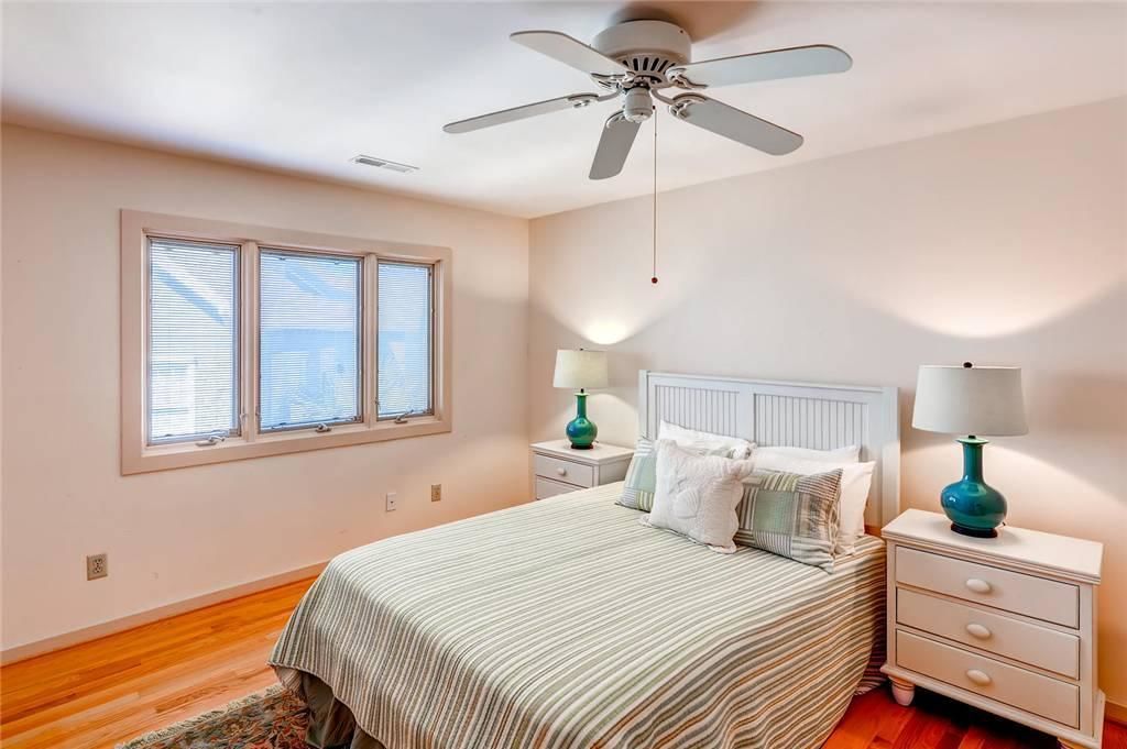Un dormitorio con cama, dos mesitas de noche, ventilador de techo y ventana con persianas.