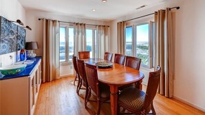 A dining area with a wooden table and chairs, large windows with curtains, and a view of the outdoors. - SeaWinds 4 Bedroom Holiday Home By Bald Head Island (Bald Head Island)
