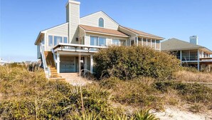 A two-story house with a large garage, a covered porch, and a chimney. - SeaWinds 4 Bedroom Holiday Home By Bald Head Island (Bald Head Island)