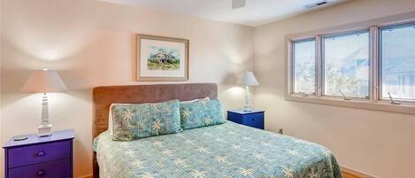 Een slaapkamer met een bed, twee nachtkastjes, een plafondventilator, een raam met zonwering en een lijst met een afbeelding aan de muur.