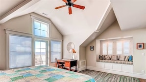 A bedroom with a large bed, a desk, a chair, a ceiling fan, a window seat, and a view of the outdoors. - Summer Island 6 Bedroom Holiday Home By Bald Head Island (Bald Head Island)