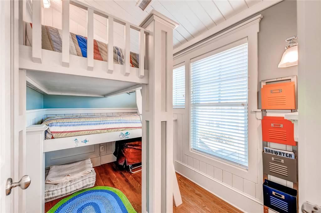 Une chambre avec des lits superposés, une fenêtre avec des stores et un meuble de rangement fixé au mur.
