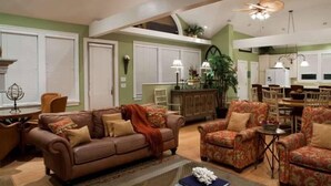 A spacious living room with a brown leather sofa, floral armchairs, and a dining area with a wooden table and chairs. - Summer House 4 Bedroom Holiday Home By Bald Head Island (Bald Head Island)
