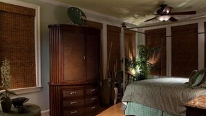 A bedroom with a large wooden wardrobe, a bed with a checkered bedspread, and a ceiling fan. - Summer House 4 Bedroom Holiday Home By Bald Head Island (Bald Head Island)