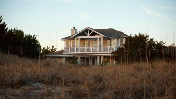 A two-story house with a balcony, surrounded by tall grasses and trees. - Summer House 4 Bedroom Holiday Home By Bald Head Island (Bald Head Island)