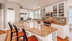 A spacious kitchen with a large island, white cabinetry, and a tiled backsplash. - Tiburon Marsh 4 Bedroom Holiday Home By Bald Head Island (Bald Head Island)