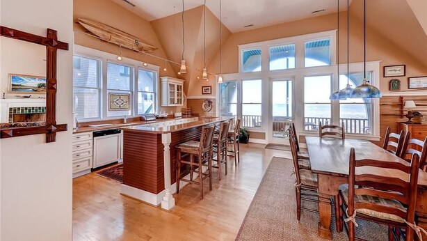 A spacious kitchen with a large island, wooden chairs, and a dining table with chairs. There are large windows providing natural light and a view of the outdoors. - Twin Peaks 3 Bedroom Holiday Home By Bald Head Island (Bald Head Island)