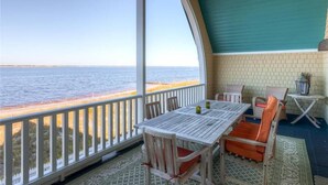 A balcony with a view of the sea, a table with chairs, and a small table with a lamp. - Twin Peaks 3 Bedroom Holiday Home By Bald Head Island (Bald Head Island)