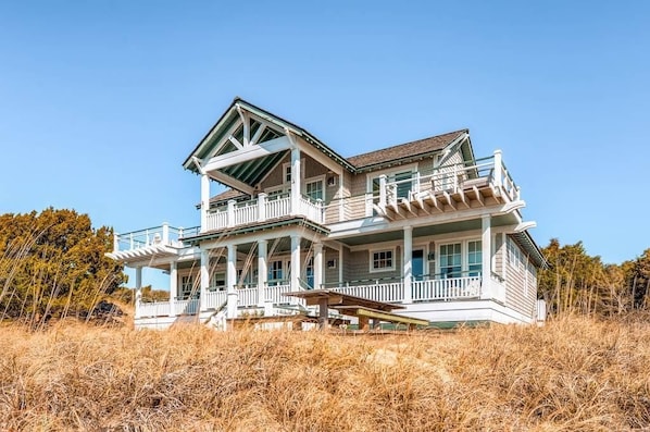 A large, two-story house with a prominent porch and multiple windows, surrounded by dry grass and trees.