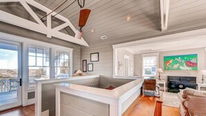 A spacious living area with a large window, a fireplace, and a kitchen area with a built-in island. - Watch Hill 5 Bedroom Holiday Home By Bald Head Island (Bald Head Island)
