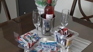 Une table à manger avec une bouteille de vin, deux verres, un plateau de collations et un vase rempli de fleurs.