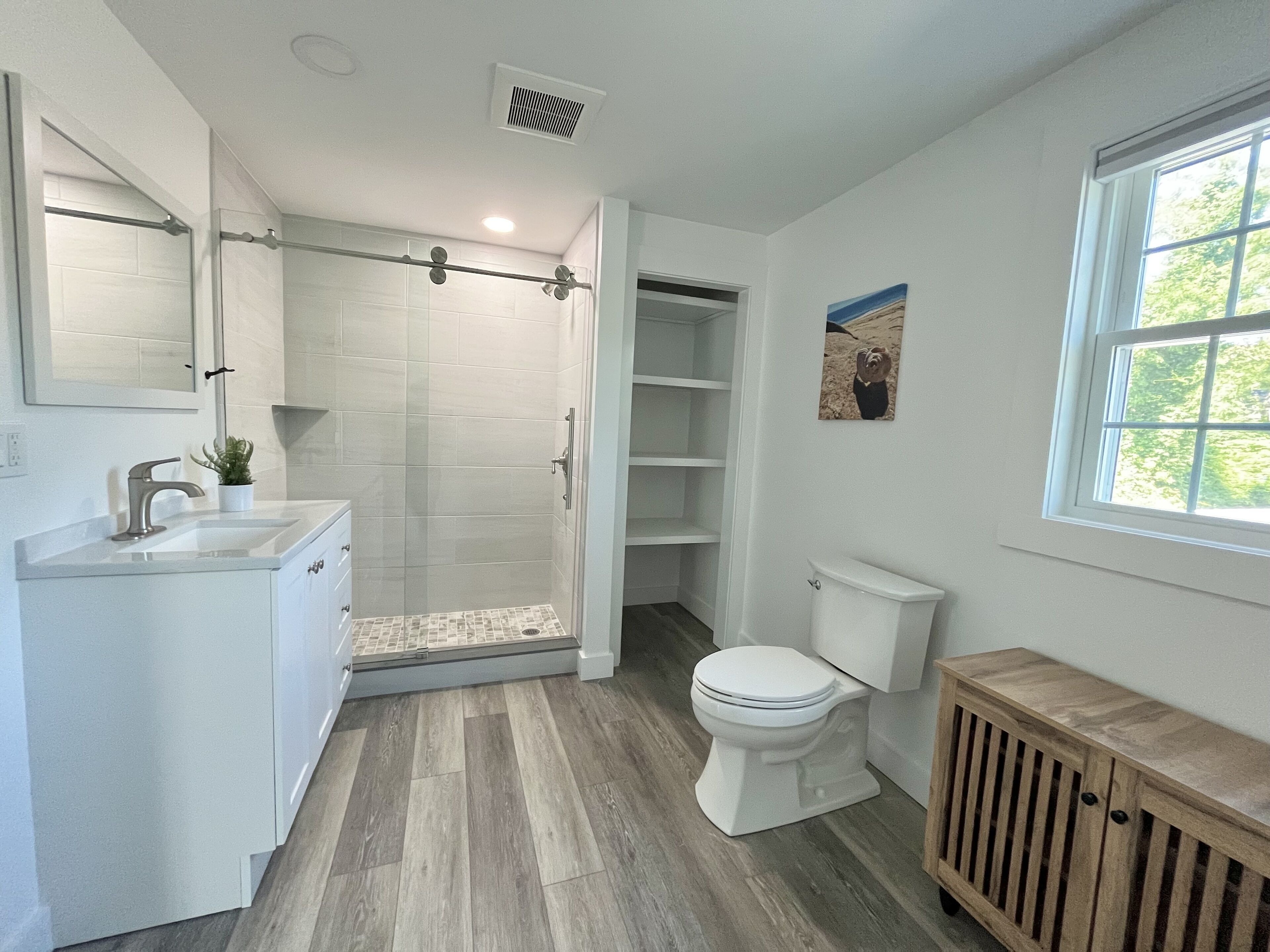 A modern bathroom with a glass shower enclosure, a white toilet, and a wooden cabinet.