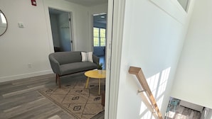 A modern living room with a grey sofa, a small yellow table, and a patterned rug. A wooden staircase leads to an upper level. - Kingfisher Lodging (Dennis)