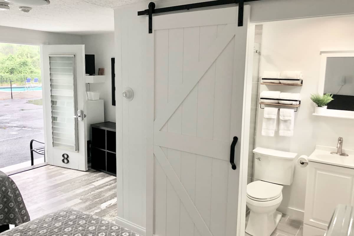 Un baño moderno con inodoro blanco, lavamanos y espejo. Una puerta corrediza estilo caserío da acceso a la zona de ducha.