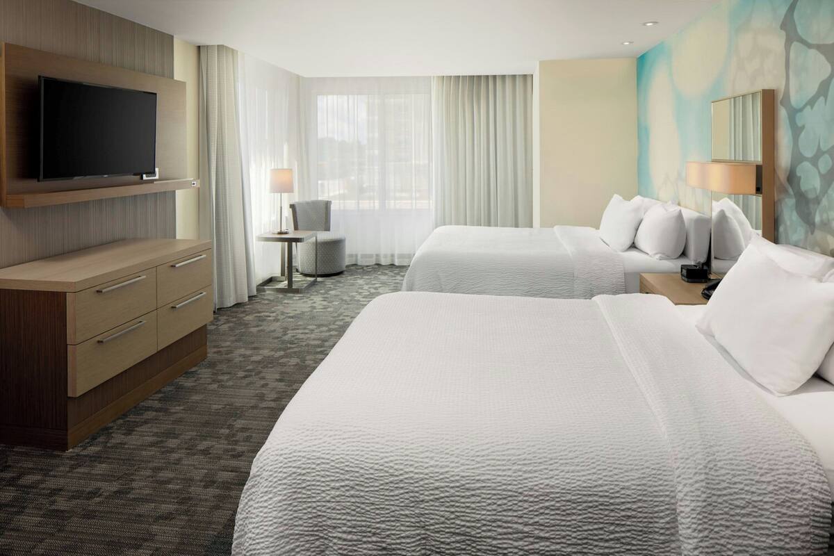 A hotel room with two beds, a TV mounted on the wall, a desk, and a chair.