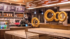 A modern bar area with a wooden counter, metal chairs, and a menu board in the background. - Courtyard by Marriott Detroit Farmington (Farmington Hills)