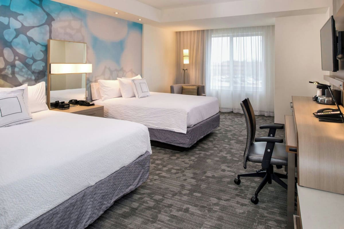 A hotel room with two beds, a desk, a chair, a TV, and a window with curtains.