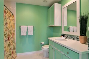 A bathroom with mint green walls, a white toilet, a white sink, and a mirror above the sink. There are two white towels hanging on the wall.