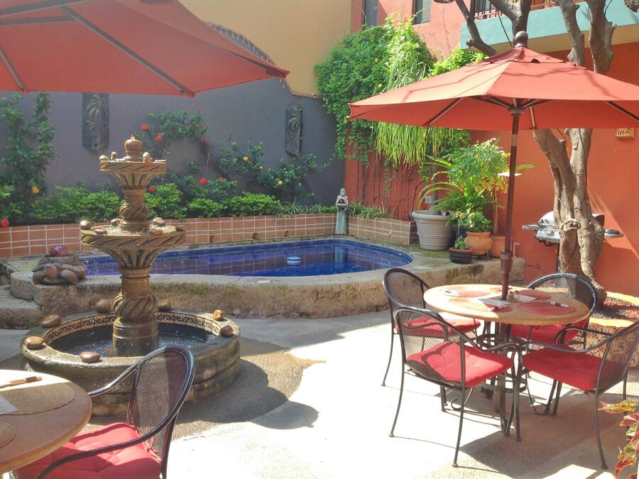 Un patio con una fuente, una piscina y mobiliario exterior con sombrillas.