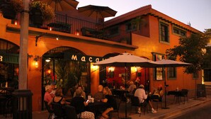 An outdoor cafe with tables and chairs, a building with a sign reading "Macau", and a street in the background.