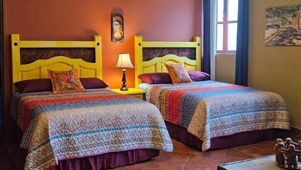 A hotel room with two beds, a chandelier, an air conditioning unit, and a small table with a decorative item. - Hotel Casa de Leyendas (Mazatlán)