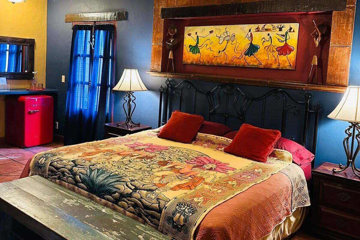 A bedroom with a bed, two bedside tables, a ceiling fan, a red refrigerator, and a wall-mounted painting.