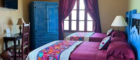 A bedroom with a bed, a ceiling fan, a window with curtains, a desk with a lamp, and a blue cabinet.