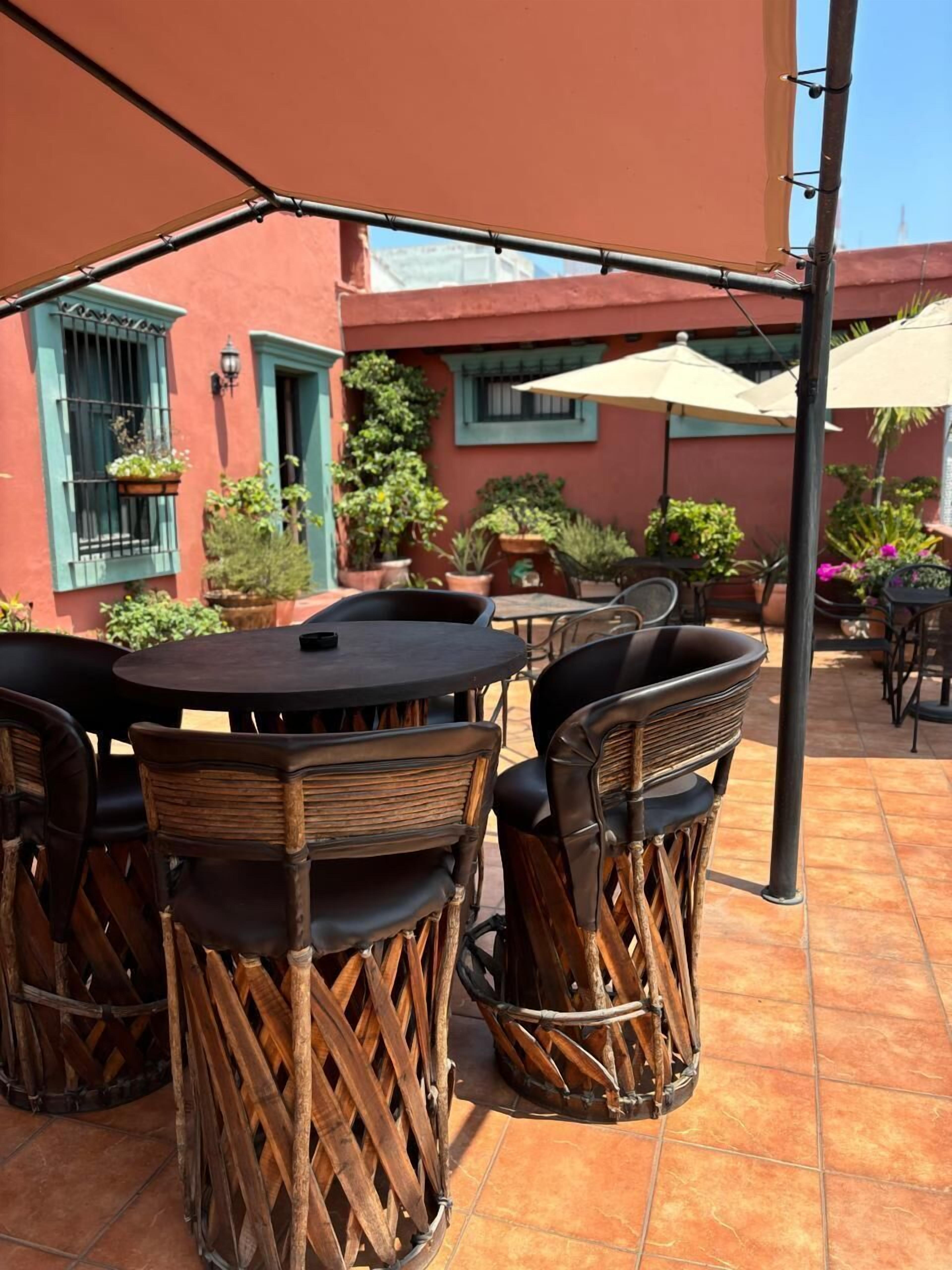 An outdoor patio with a round table and chairs, surrounded by potted plants and umbrellas.