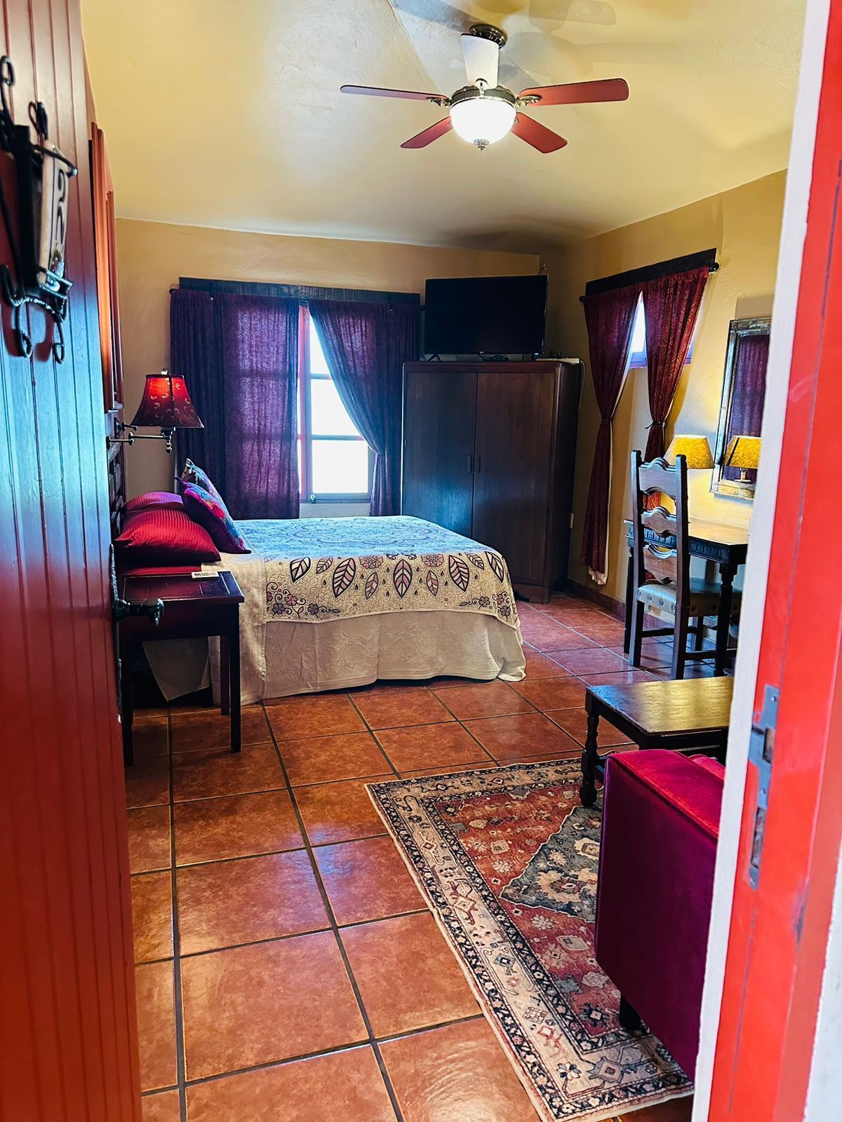 Ein Schlafzimmer mit Bett, Schreibtisch, Stuhl, Kleiderschrank, Deckenventilator und Teppich.