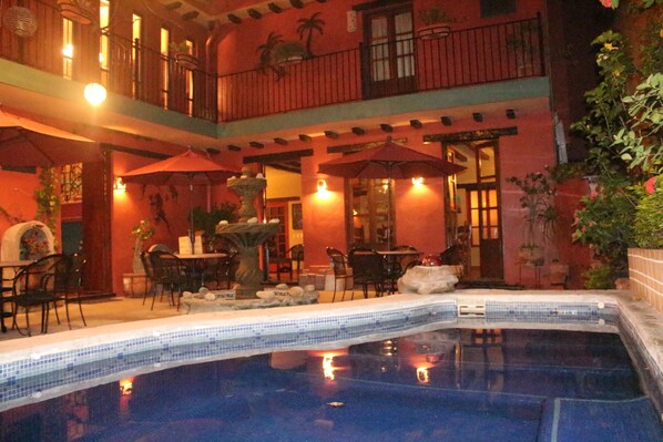 A pool area with a tiled edge, outdoor seating with umbrellas, and a building with a balcony. - Hotel Casa de Leyendas (Mazatlán)
