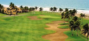 Campo de golf con vista al mar, palmeras y un edificio al fondo.