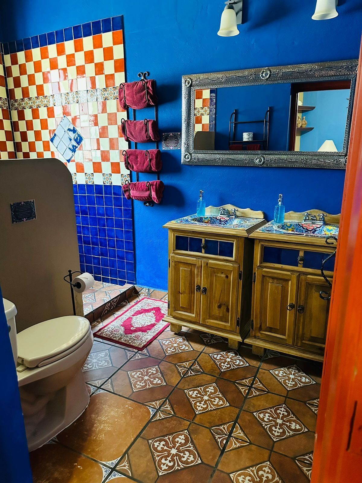 A bathroom with a blue tiled wall, a checkered tile backsplash, a wooden vanity with a mirror, and a toilet.