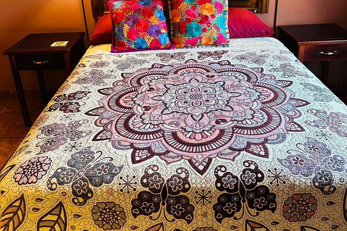 A hotel room with a bed, two nightstands, a lamp, a colorful pillow, and a painting on the wall.