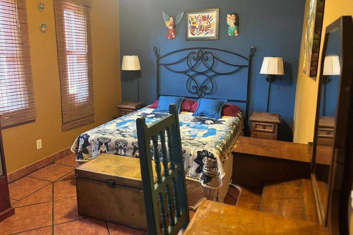 A bedroom with a bed, two bedside tables, a chair, and a window with blinds.