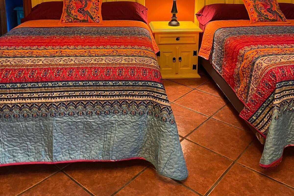 A room with two beds, each with a patterned bedspread, a nightstand with a lamp, and a wall-mounted artwork.