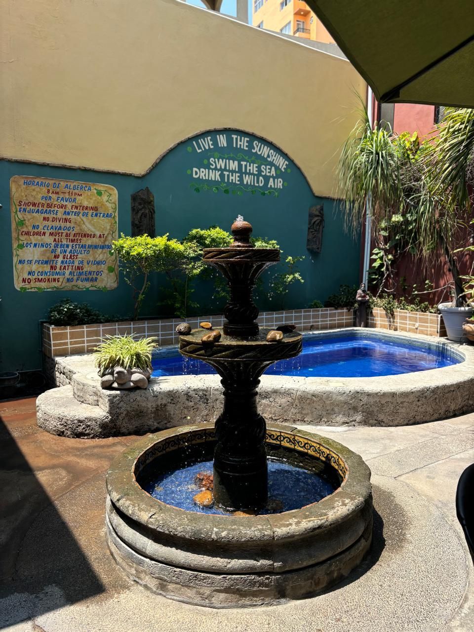 A fountain with a sign above it, a pool, and a wall with text.