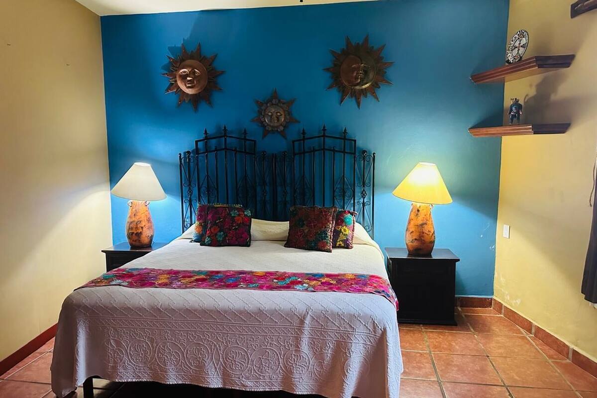 A bedroom with a bed, two nightstands, a blue wall with decorative sun motifs, and a tiled floor.