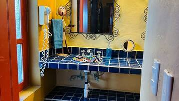 Un baño con pared amarilla, lavamanos con azulejos azules, espejo con marco decorativo, secador de pelo y toallero.