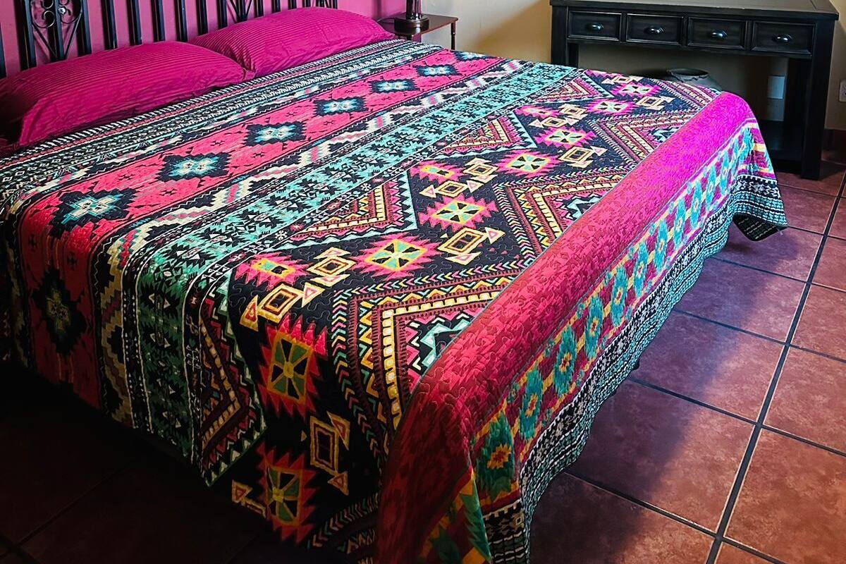 A bed with a colorful patterned bedspread, a black metal headboard, and a nightstand with a lamp.