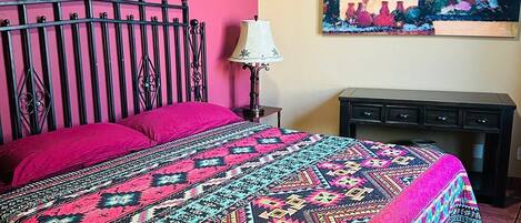 Una cama con una colcha estampada de colores, un cabecero de metal negro y una mesita de noche con una lámpara.