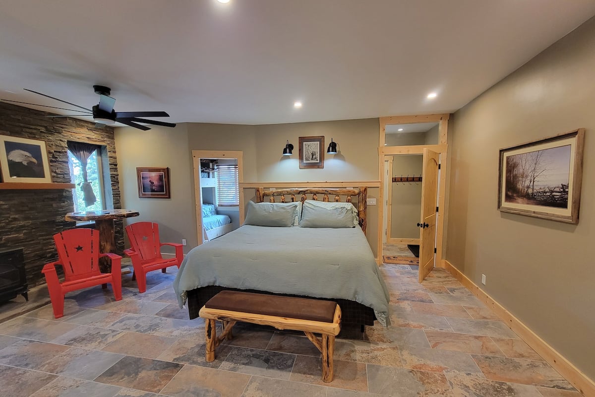 Ein Schlafzimmer mit einem Bett, einer hölzernen Bank, einem roten Sessel, einer Steinwand und einem Deckenventilator.