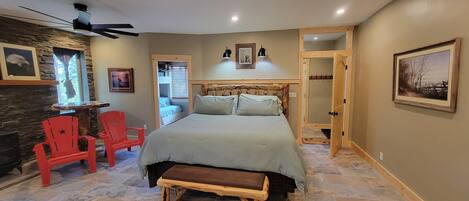 A bedroom with a bed, a wooden bench, a red chair, a stone wall, and a ceiling fan.