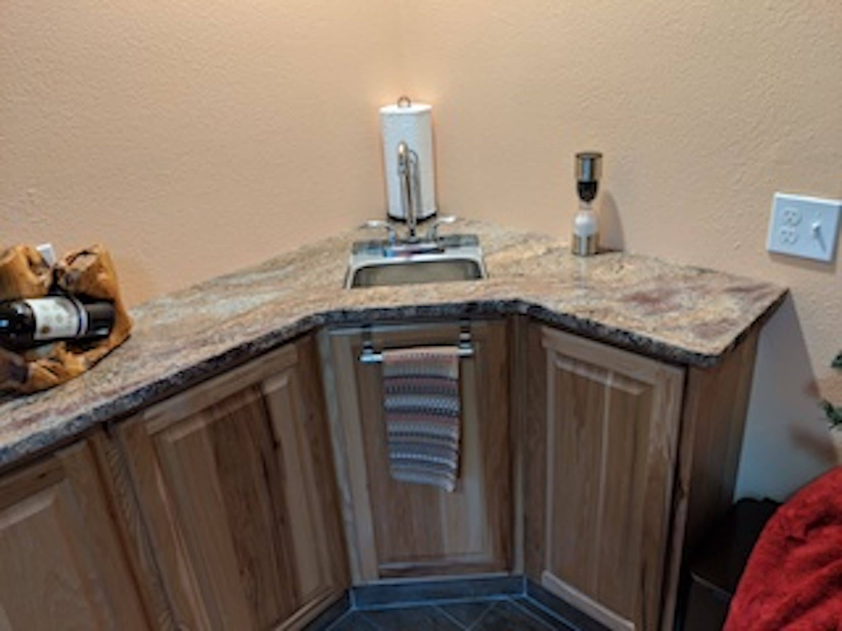 A corner kitchen with wooden cabinets, a granite countertop, a sink, and a towel rack.