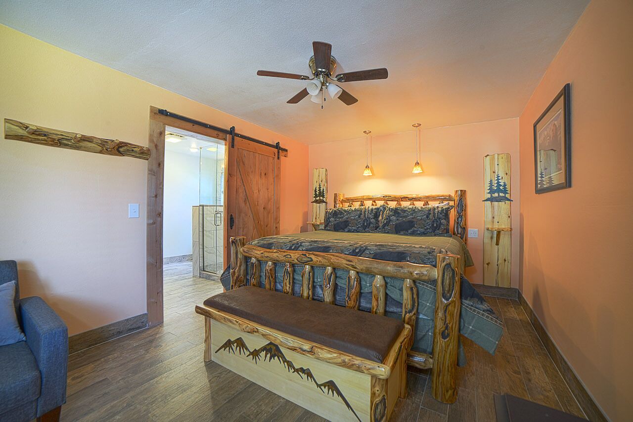 Une chambre avec un lit en bois, un banc, un ventilateur de plafond et une vue sur un balcon.