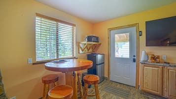 A compact kitchen with a wooden table and stools, a refrigerator, and a microwave on a small shelf.