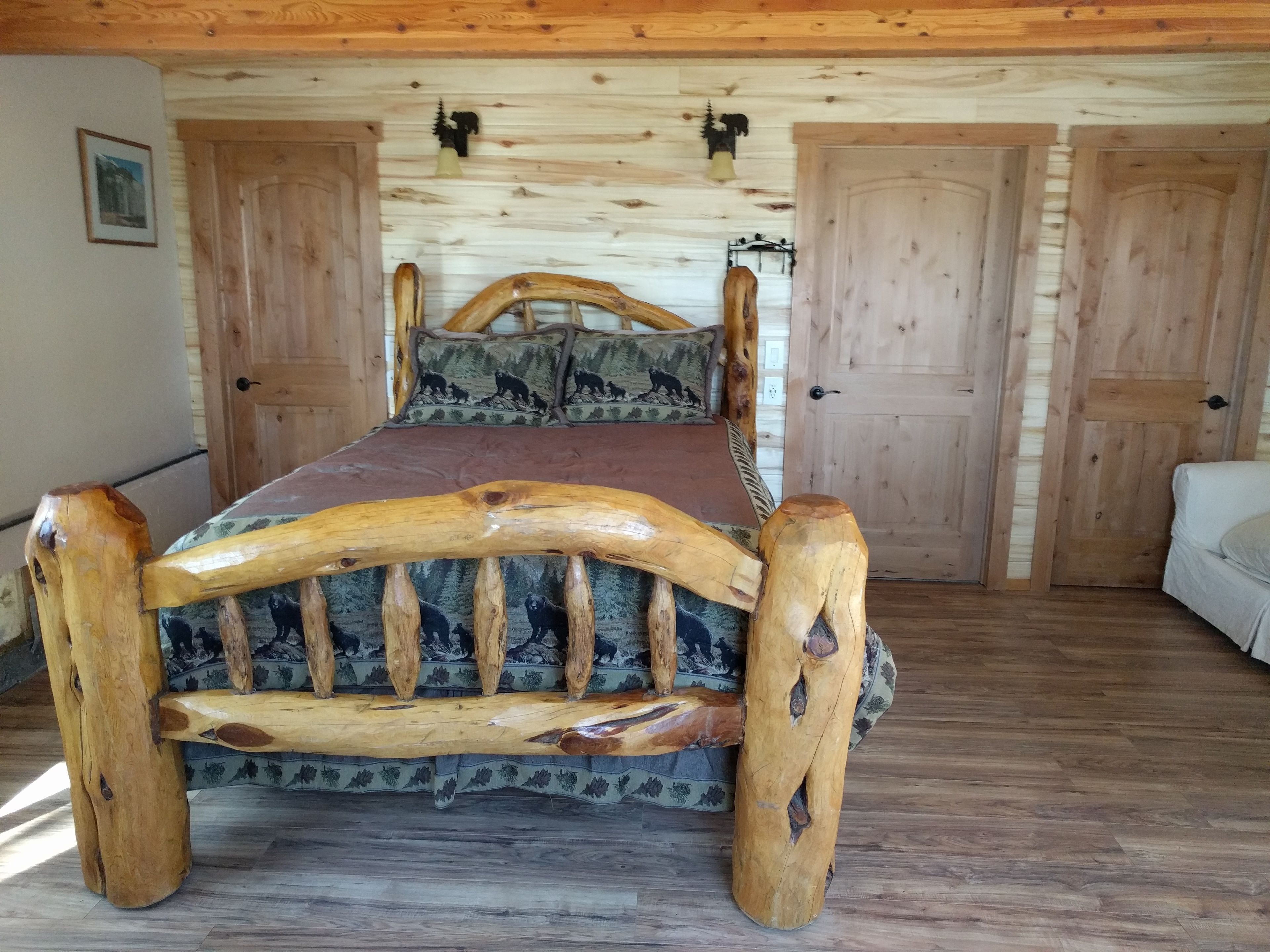 A wooden bed with a unique headboard design, a wooden floor, and a white wall with a picture.
