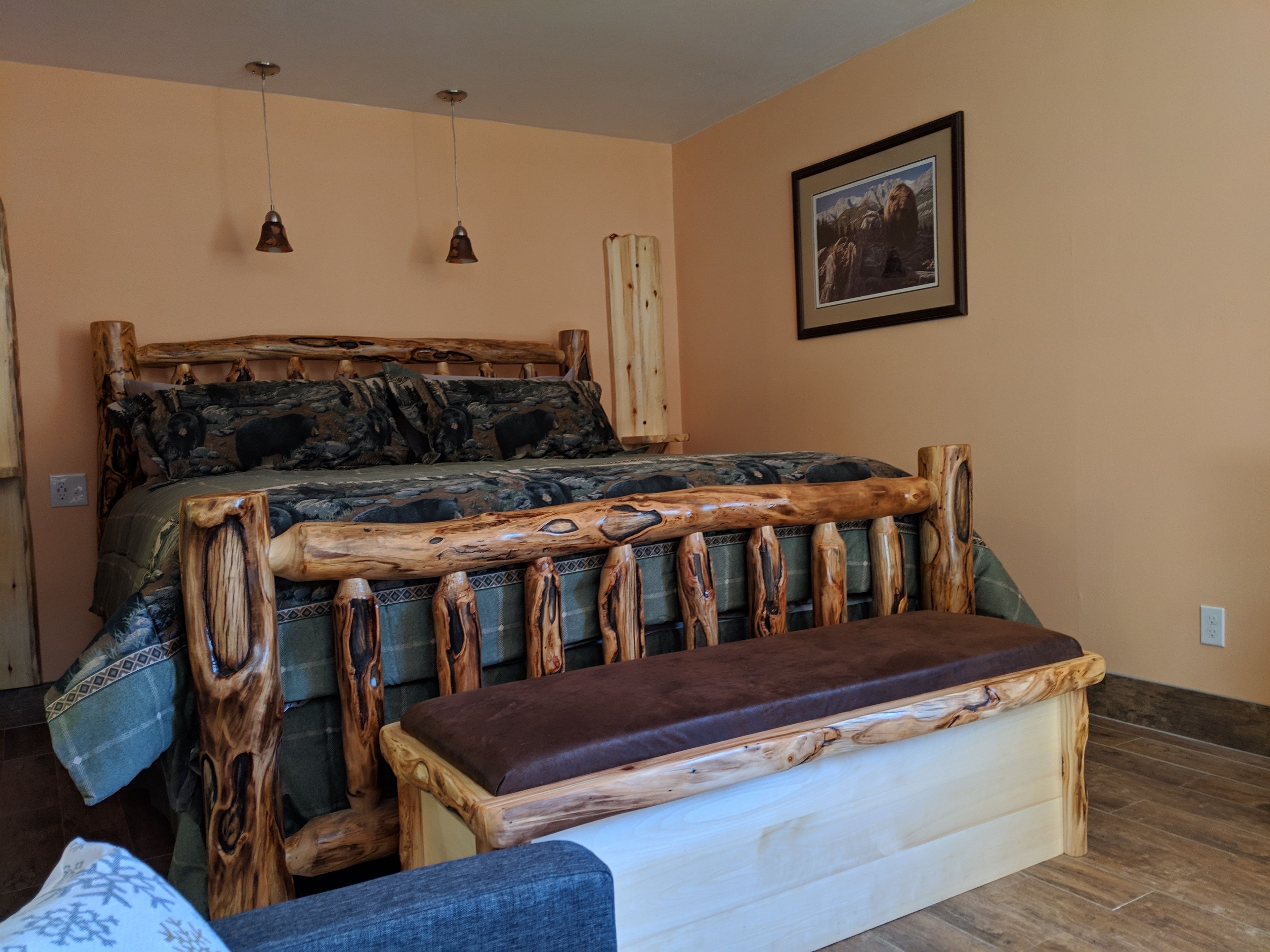 Een slaapkamer met een houten bedframe, een bankje en een ingelijst schilderij aan de muur.