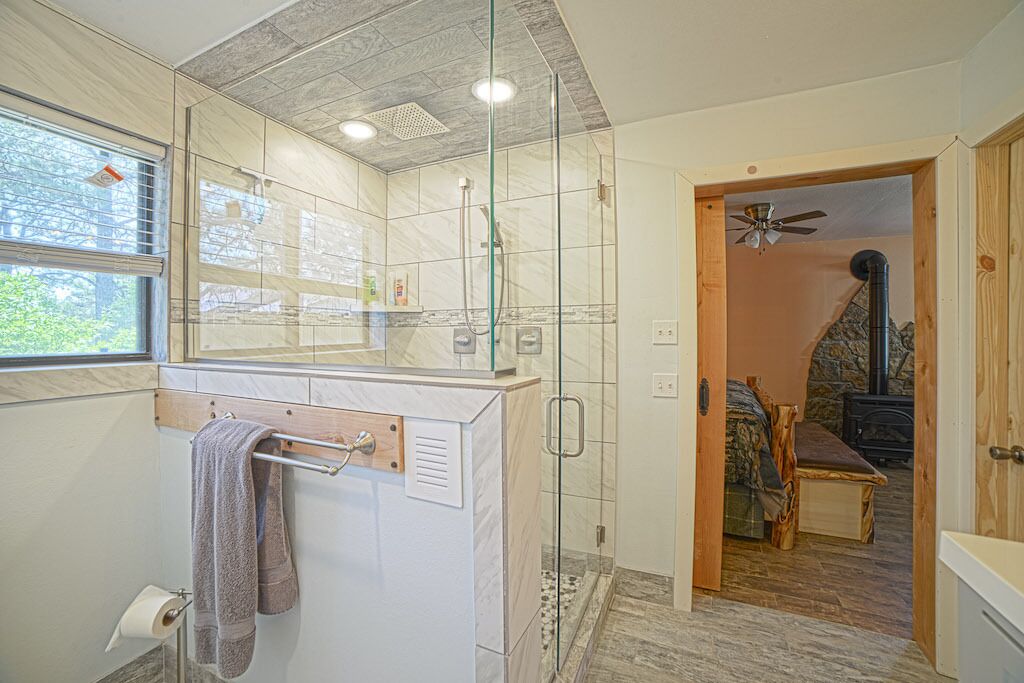 Une salle de bain moderne avec une douche à l’italienne en verre, un banc en bois et une cheminée visible dans la pièce adjacente.